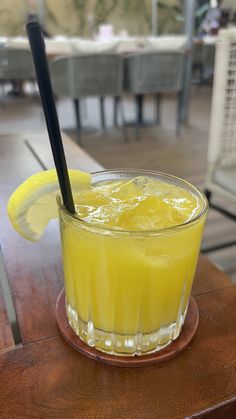 a glass filled with lemonade sitting on top of a wooden table next to a black straw