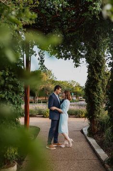 a man and woman standing under an arch in the middle of a walkway surrounded by greenery