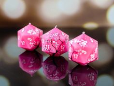 three pink dices sitting on top of a black table next to each other with numbers painted on them