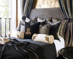 a large bed sitting next to a window covered in black and gold pillows on top of a wooden floor