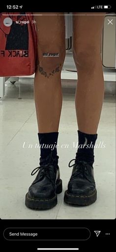 the legs and ankles of a person wearing black boots with tattoos on them, standing in front of a luggage bag