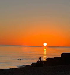 the sun is setting over the ocean with people swimming