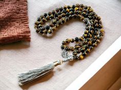 "This beautiful hand-knotted, Tiger's Eye Mala, is made with high-quality, 8mm crystal beads.  It measures approximately 25\" in length, with a gold tassel and tree of life charm.  Each Mala Necklace comes with an intuitively chosen bracelet, that will compliment your necklace, as a free gift. Tiger's Eye is good for growing your confidence, strength, and courage.  It helps you get centered and calm, motivating your energy.  Tiger's Eye is effective in helping you confront your fears, doubts, an Hand Knotted Adjustable Beads As A Gift, Adjustable Hand-knotted Beads As A Gift, Adjustable Hand-knotted Beads For Gifts, Brown Beaded Mala For Rituals, Brown Beaded Spiritual Mala, Brown Polished Beads Spiritual Mala, Brown Wooden Beads Spiritual Mala, Adjustable Brown Hand-strung Mala, Gift Tree