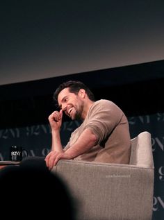 a man sitting in a chair with his hand on his chin and smiling at the camera