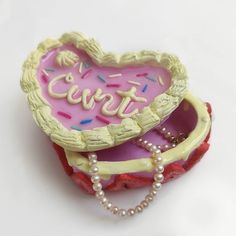 a pink heart shaped box sitting on top of a white table next to a beaded necklace