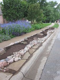 there is a long row of rocks on the side of the road with blue flowers in the background