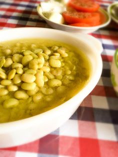 a white bowl filled with green beans on top of a checkered table cloth next to bowls of vegetables