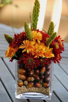 a clear vase filled with lots of flowers and nuts on top of a wooden table