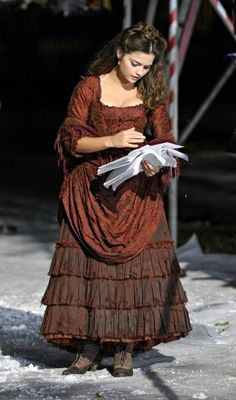 a woman in an old fashioned dress is reading a piece of paper while standing in the snow