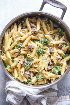 a pot filled with pasta and broccoli on top of a table next to a towel