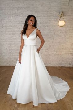 a woman wearing a white wedding dress standing in front of a brick wall with her hands on her hips