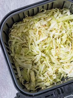 shredded cabbage in a black plastic container on a white tableclothed surface, ready to be cooked