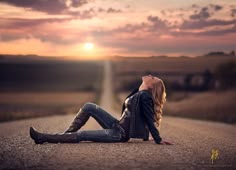 a woman sitting on the side of a road at sunset