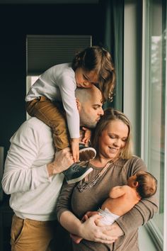 a man and woman holding a baby while standing next to a window