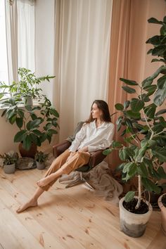 a woman sitting in a chair next to a potted plant on the floor near a window