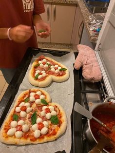 two uncooked pizzas sitting on top of a stove next to a pan