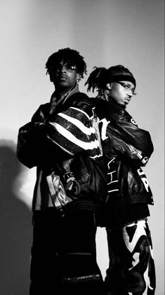 two young men standing next to each other in front of a white wall and wearing leather jackets