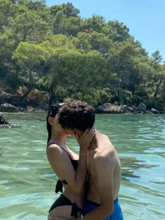 a man and woman kissing in the water at the beach with trees in the background