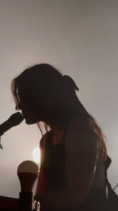 the silhouette of a woman holding a microphone in front of her face and looking down