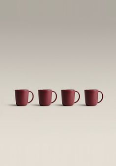 three red coffee mugs lined up in a row on a gray background with one empty