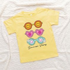 Looking for a cute tee for your kids? We have the perfect Sunnies Summer Vibes graphic tee addition to their closet! Also available in youth tees. Trendy Cotton T-shirt For Playwear, Playful Cartoon Print T-shirt For Playwear, Yellow Cartoon Print T-shirt For Summer, Summer Cartoon Print Playwear T-shirt, Fun Graphic Print T-shirt For Playwear, Trendy Character Print T-shirt For Spring, Trendy Spring T-shirt With Character Print, Summer Cartoon Print T-shirt, Summer Short Sleeve Cartoon Print T-shirt