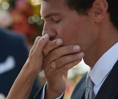 a close up of a person wearing a suit and tie holding his hand to his face