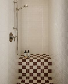 a tiled shower stall with brown and white tiles on the floor, along with two soap dispensers