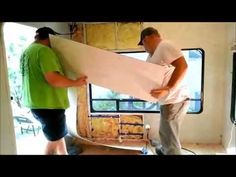 two men standing in front of a window holding up a large sheet of white paper