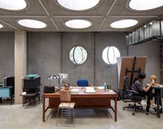 a person sitting at a desk in an office with round windows above the room and below them