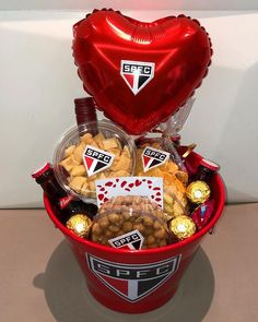 a red bucket filled with lots of chocolates and nuts next to a heart shaped balloon