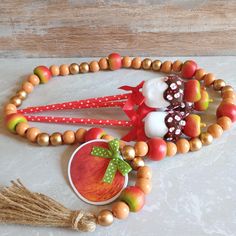 a wooden beaded necklace with an apple and other beads on it, next to a cup