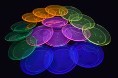 neon colored plastic discs are stacked on top of each other in the dark, with black background