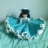 a crocheted doll is laying on a bed with a blue dress and bonnet