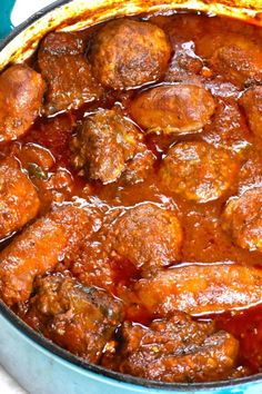 meatballs and gravy in a blue pot on a white tablecloth with spoons