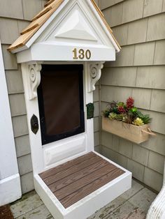 a white birdhouse with a brown roof and numbers on the front door is next to a planter