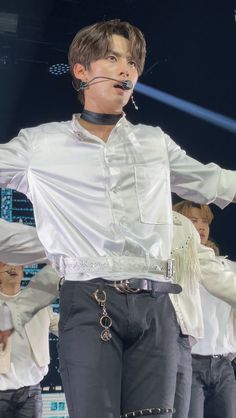 a man in white shirt and black pants on stage with his hands out to the side