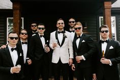 a group of men standing next to each other wearing suits and sunglasses with drinks in their hands