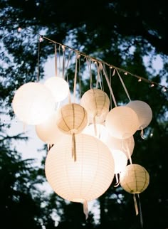 white paper lanterns hanging from strings in front of trees