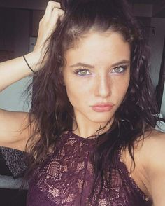 a beautiful young woman with blue eyes and brown hair wearing a purple top posing for the camera