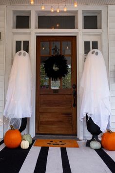 two halloween decorations on the front porch of a house with pumpkins and ghost heads