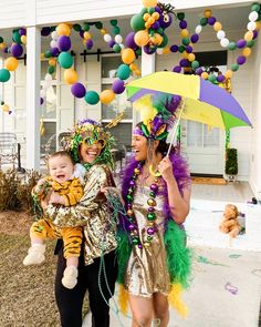 two women and a baby are dressed up for mardi gras in front of a house