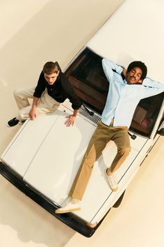 two men leaning on the hood of a white car with their hands in the air