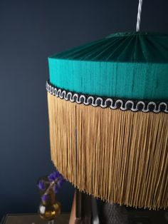 a green lamp shade sitting on top of a table next to a vase with purple flowers