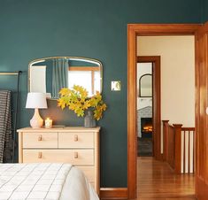 a bedroom with green walls and wooden floors, white bedding and dressers in the foreground