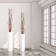 two tall white vases with branches in them on a marble floor next to a window