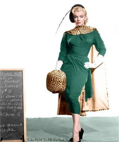 a woman in a green dress and leopard print hat standing next to a chalkboard