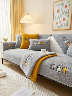 a grey couch with yellow and white pillows in a living room next to a window