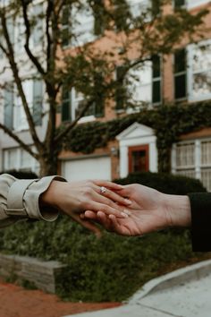 two people holding each other's hands in front of a building with trees and bushes