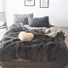 the bed is made up with fluffy grey blankets and pillows on it, along with two framed pictures