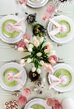 the table is set with pink and white plates, napkins, silverware, and tulips